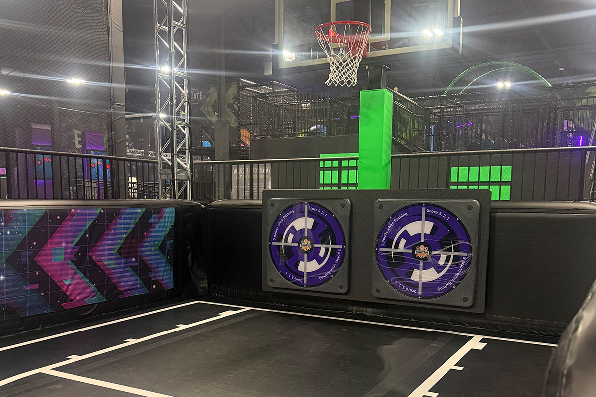 Indoor trampoline basketball court with a hoop, padded walls, and two circular target panels.