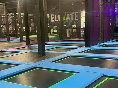 Grid of rectangular trampolines with blue padding and green borders inside an indoor trampoline park.