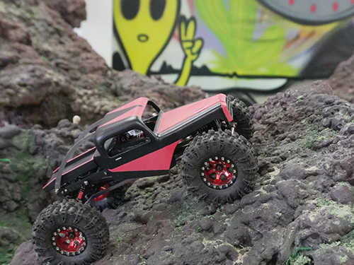 Red-and-black remote-controlled rock crawler climbing over a rugged artificial rock course.